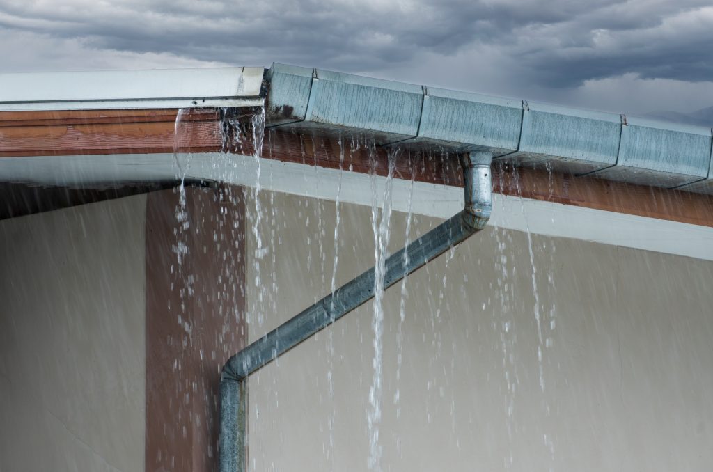Rainwater overflowing from a residential roof gutter during heavy rainfall.